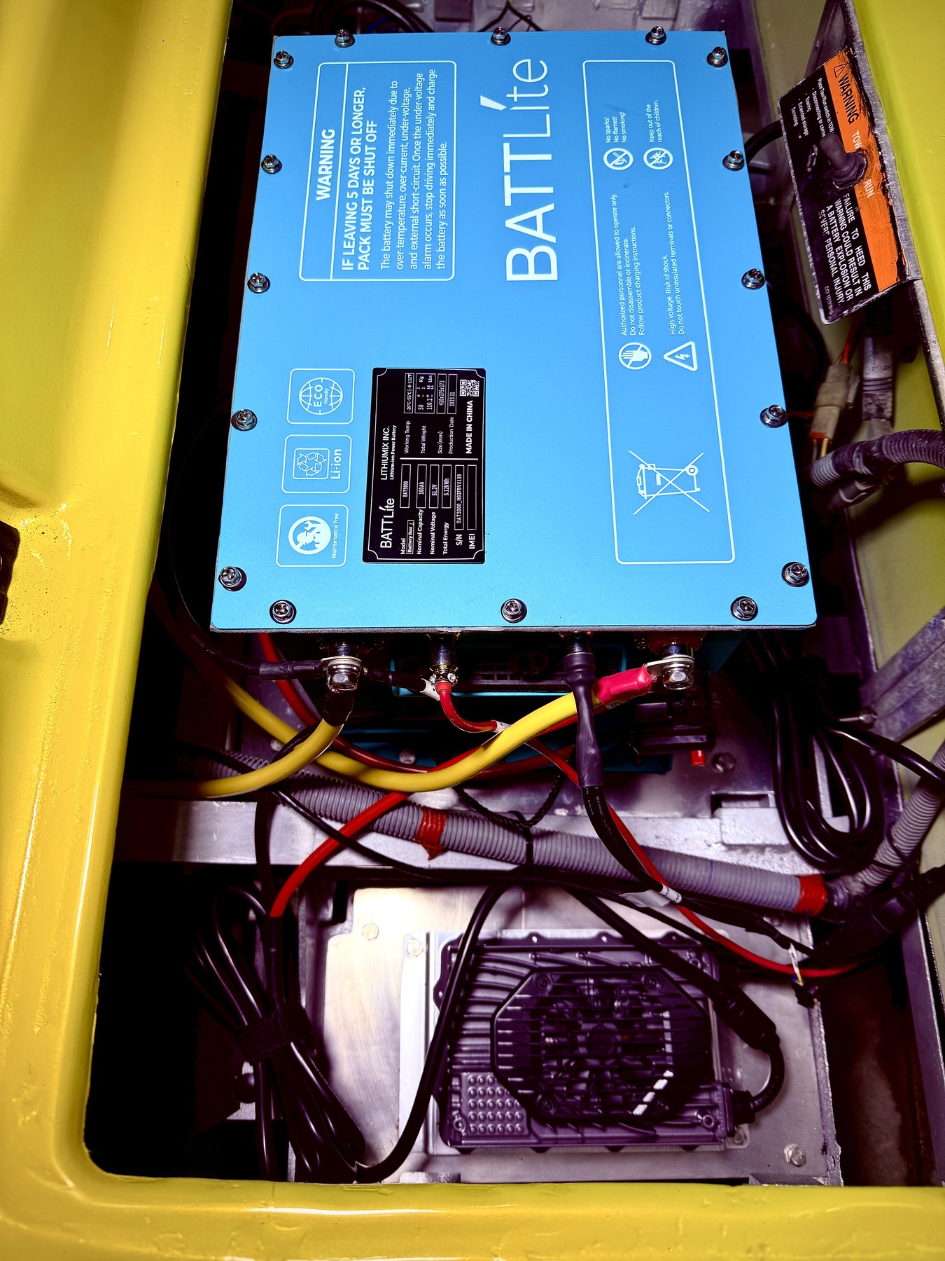 Blue BATTLite lithium battery installed in a yellow golf cart with organized power cables and controller